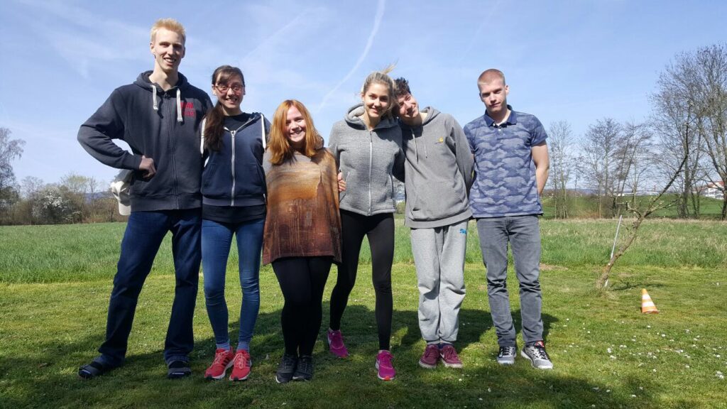 Six Camphill alumni stand in a grassy area smiling together