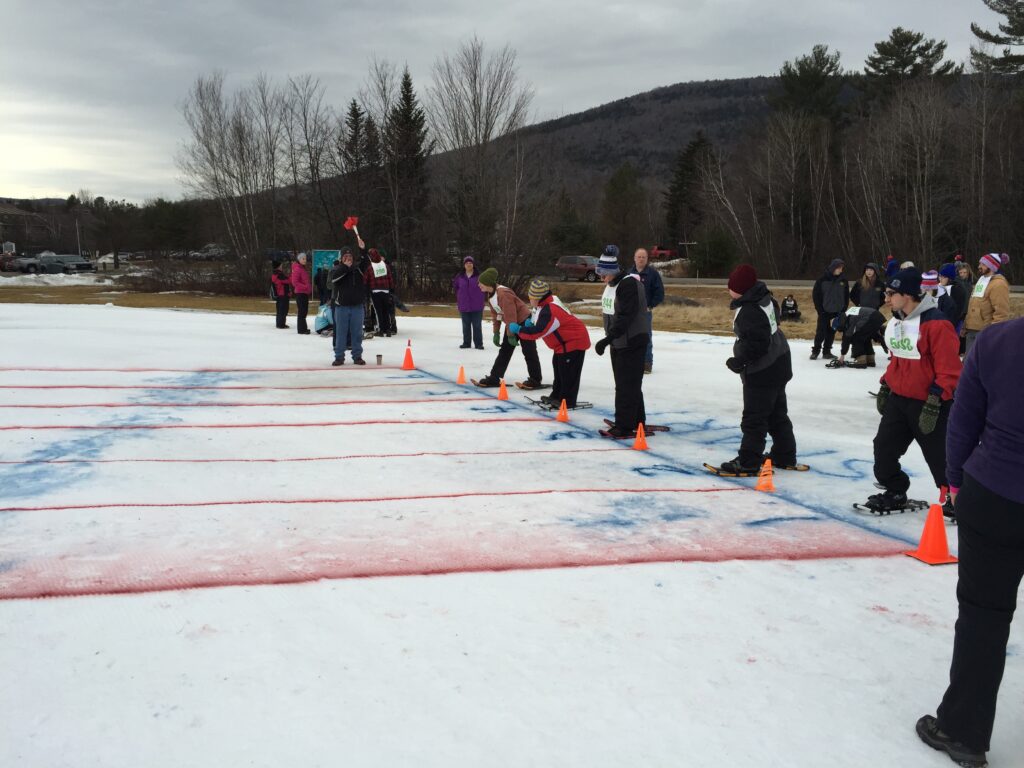Crowd of people in snowshoes line up to walk across painted lines in the snow.