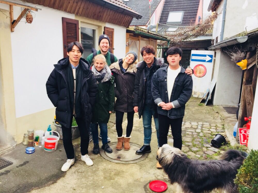 Six people standing together and smiling at the camera with a dog in the foreground, looking at them